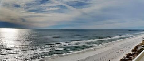 A beach view with a clear sky, ocean waves, and a distant pier.