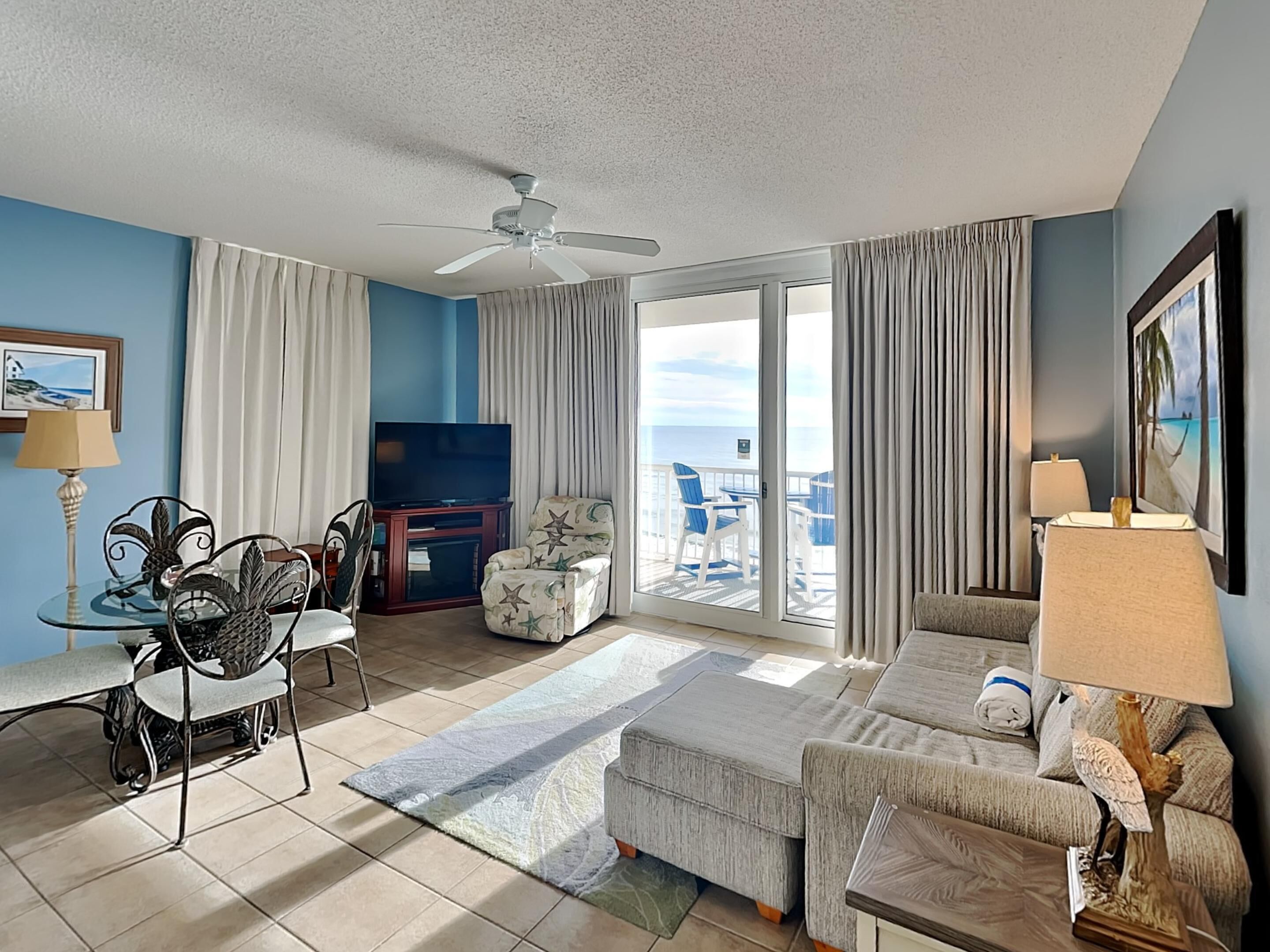 A hotel room with a balcony, a TV, a dining area with chairs, a sofa, and a lamp.