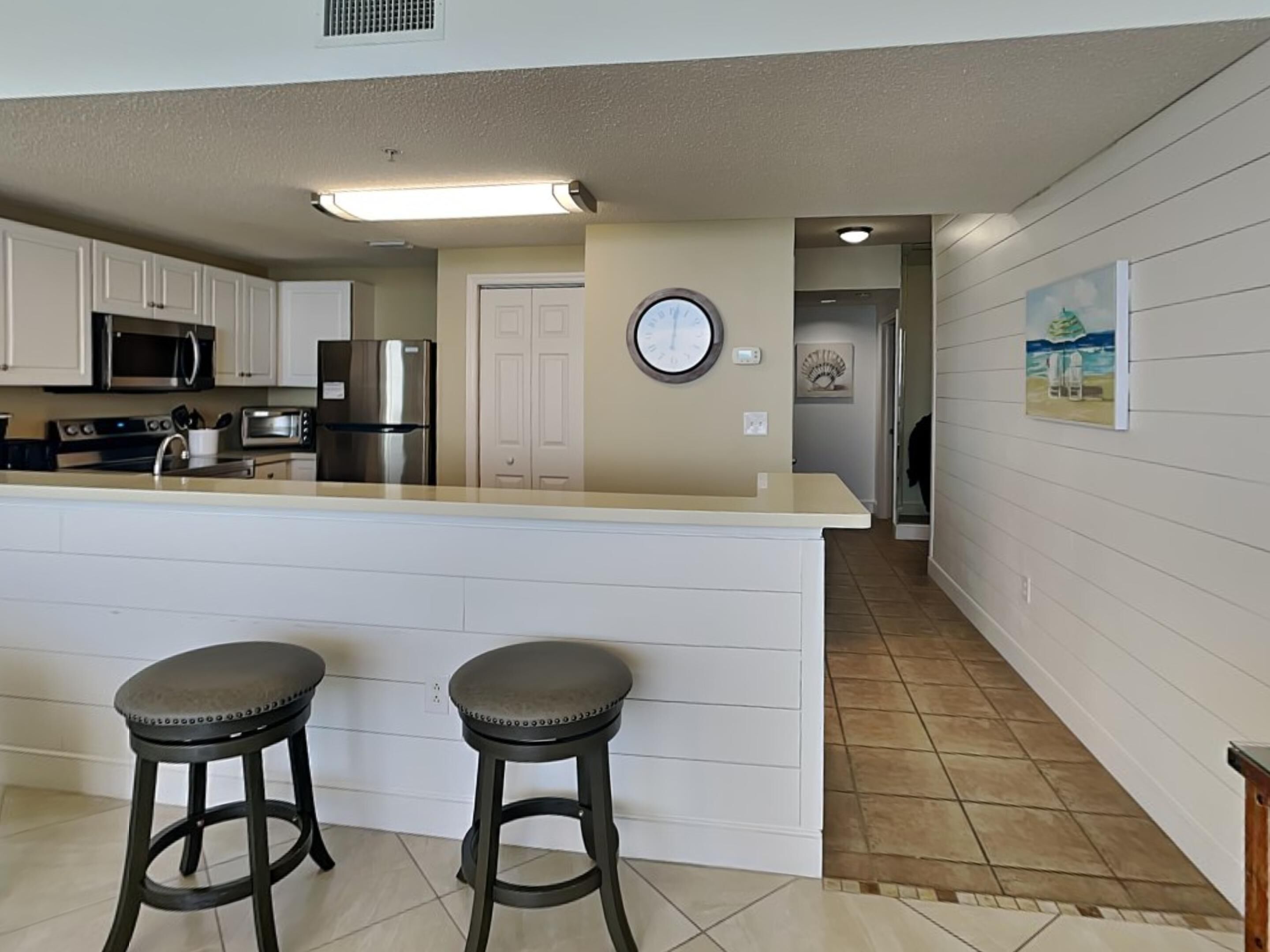 A kitchen with white cabinets, stainless steel appliances, a large island with stools, and a clock on the wall.