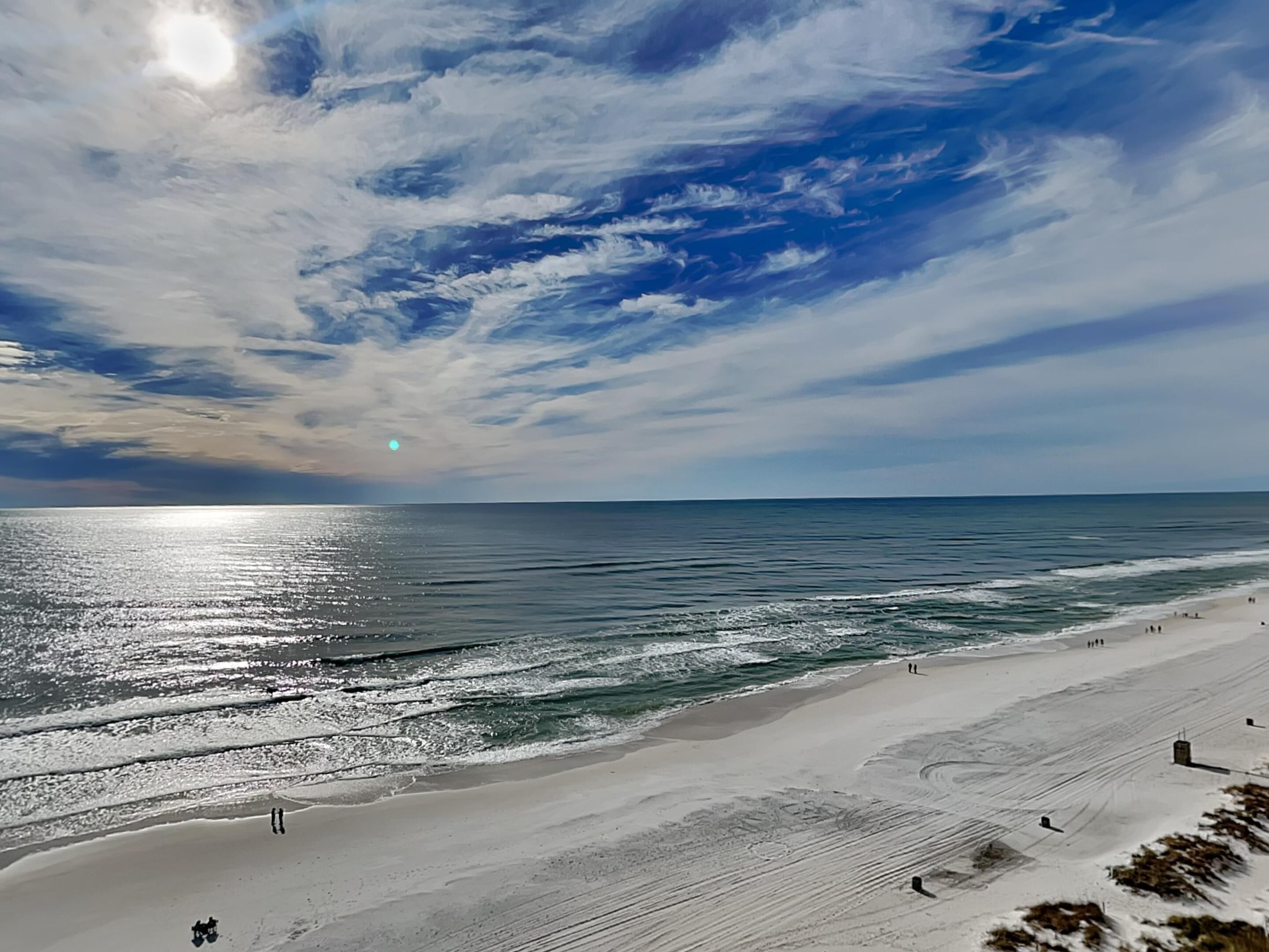 A beach with a clear sky, calm sea, and a few people walking.
