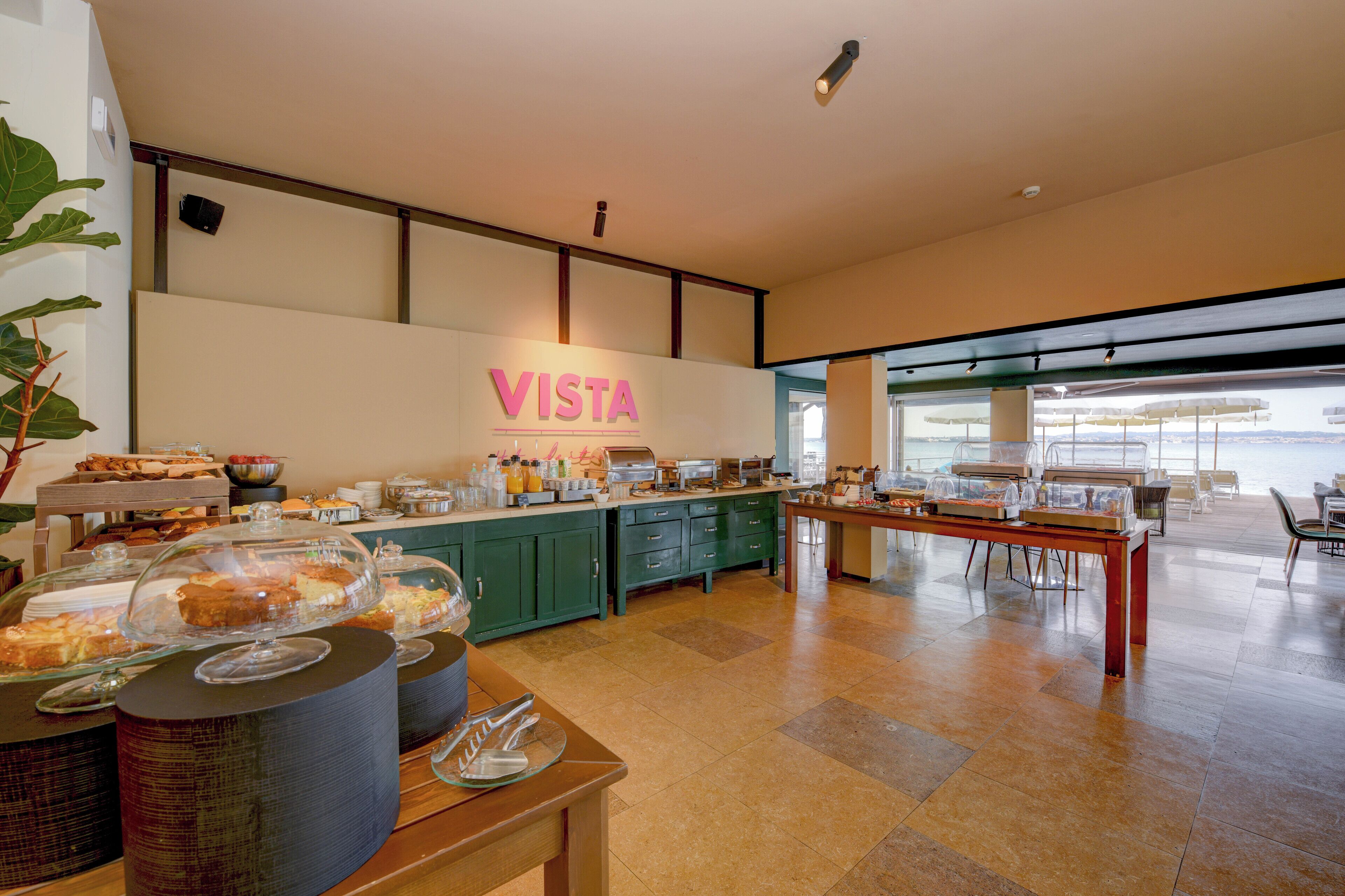 A buffet area with a 'VISTA' sign, green cabinets, and a view through the glass wall.