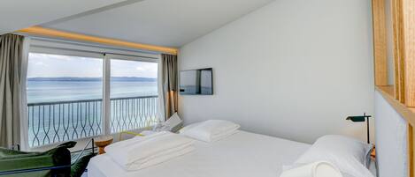 Habitación de hotel con una cama grande, vista al mar, una mesita y una silla.