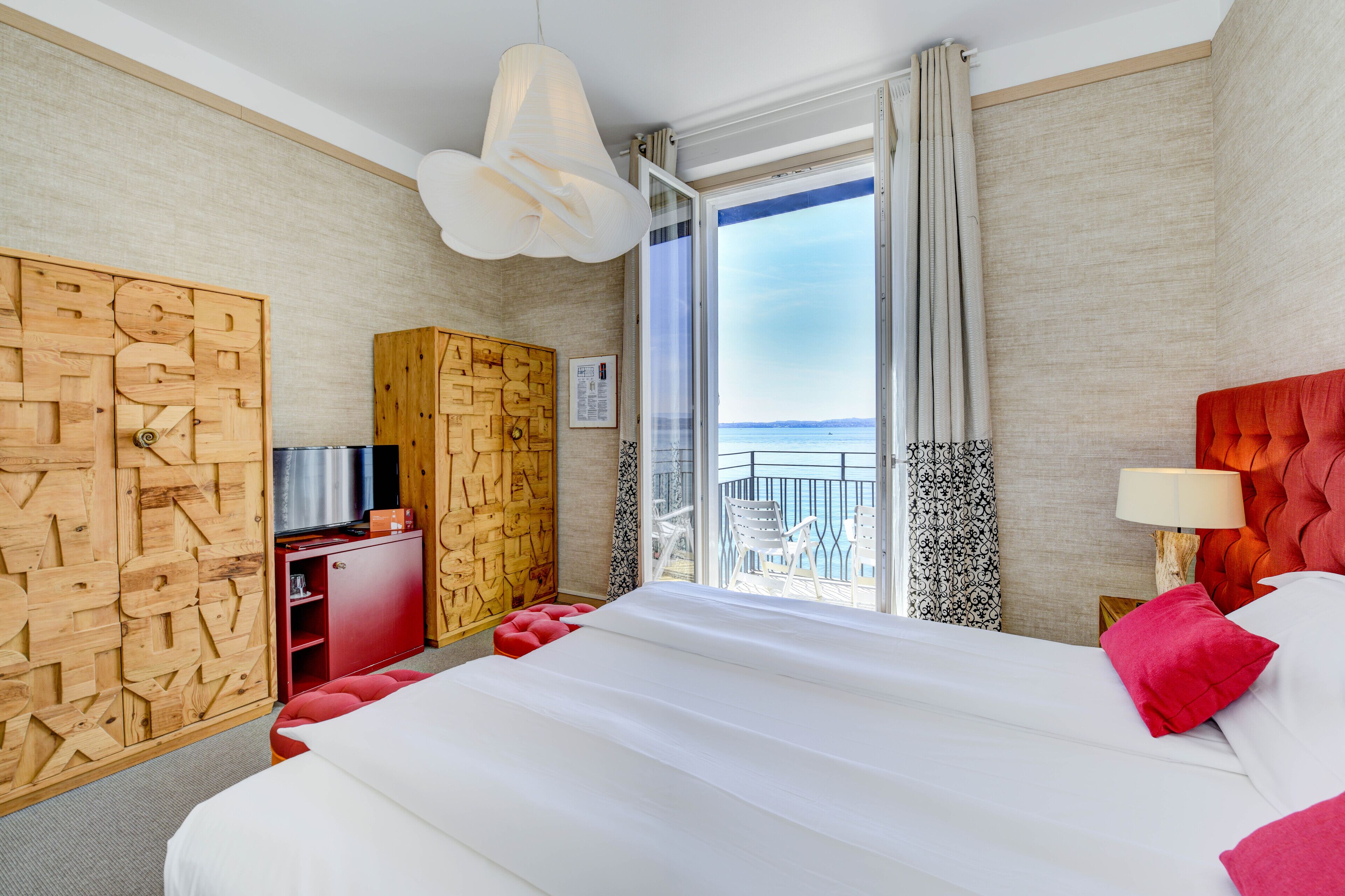 A hotel room with a large bed, a TV, a wooden wardrobe, and a balcony with a view.