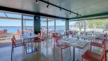 Un espace extérieur aménagé pour les repas, avec des tables et des chaises, de grandes fenêtres et une vue sur l’eau.