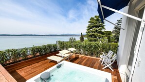 A wooden deck with a hot tub, lounge chairs, and a view of the lake. - Hotel Flaminia (Sirmione)