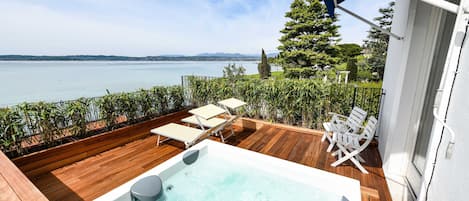 A wooden deck with a hot tub, lounge chairs, and a view of the lake.