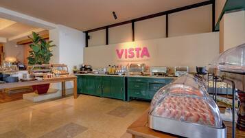 Zona de desayuno tipo buffet con un letrero 'VISTA', armarios verdes y una variedad de alimentos.