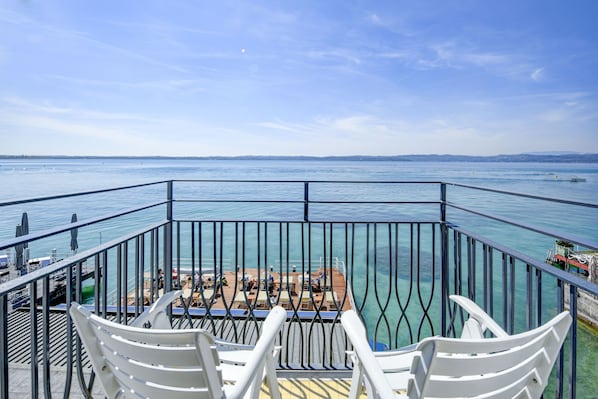 A balcony with white chairs and a table overlooking a body of water. - Hotel Flaminia (Sirmione)