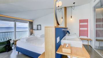 Ein modernes Hotelzimmer mit einem großen Bett, einem Holfnachtkästchen, einem integrierten Waschbecken und Meerblick.
