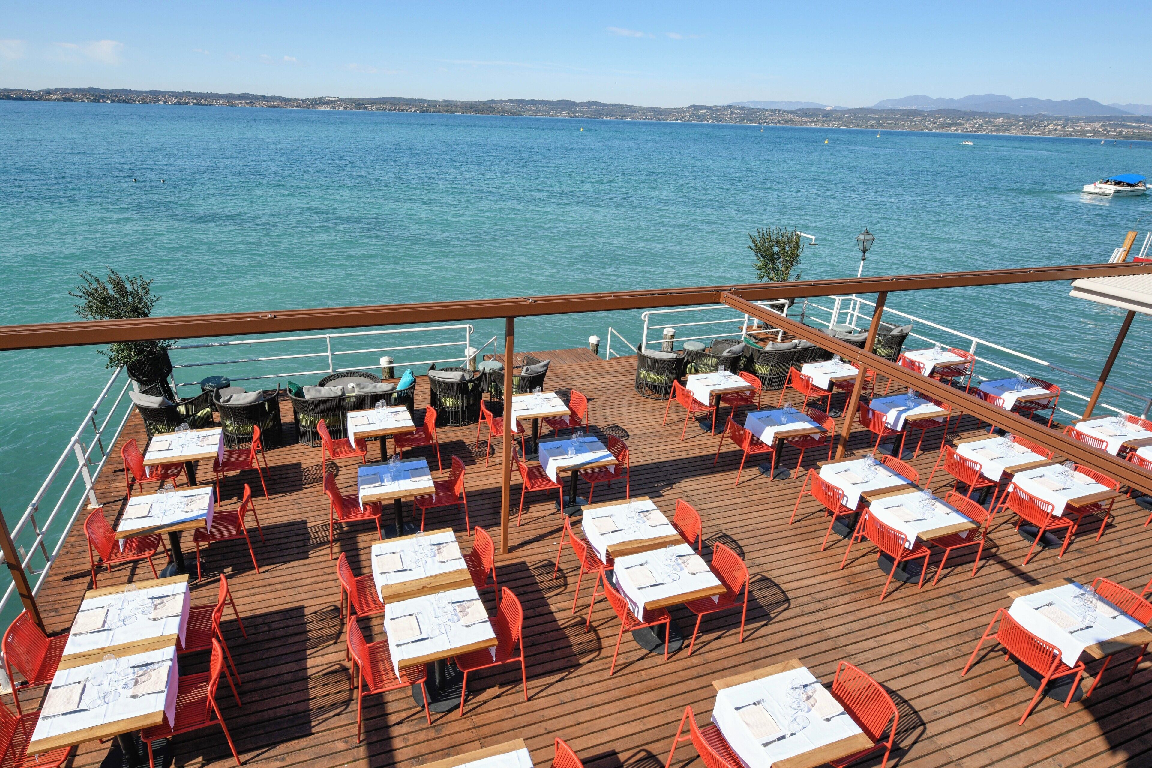 A deck with tables and chairs, overlooking a body of water with boats.
