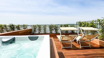 A rooftop pool area with a hot tub, two sun loungers, and a wooden deck.