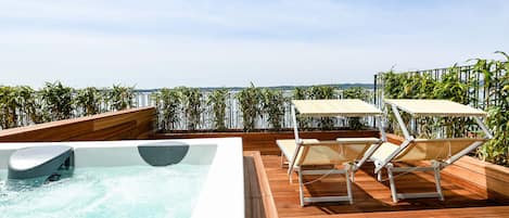 A rooftop pool area with a hot tub, two sun loungers, and a wooden deck.