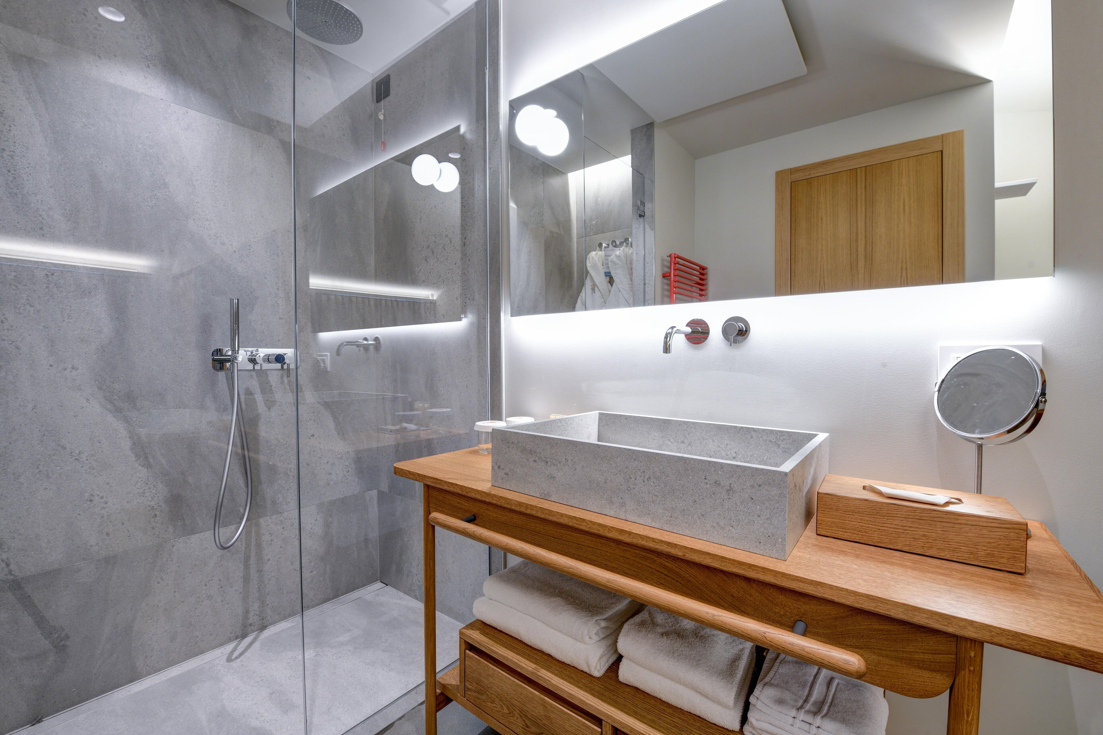 A modern bathroom with a glass shower enclosure, a wooden vanity with a large basin, and a mirror.