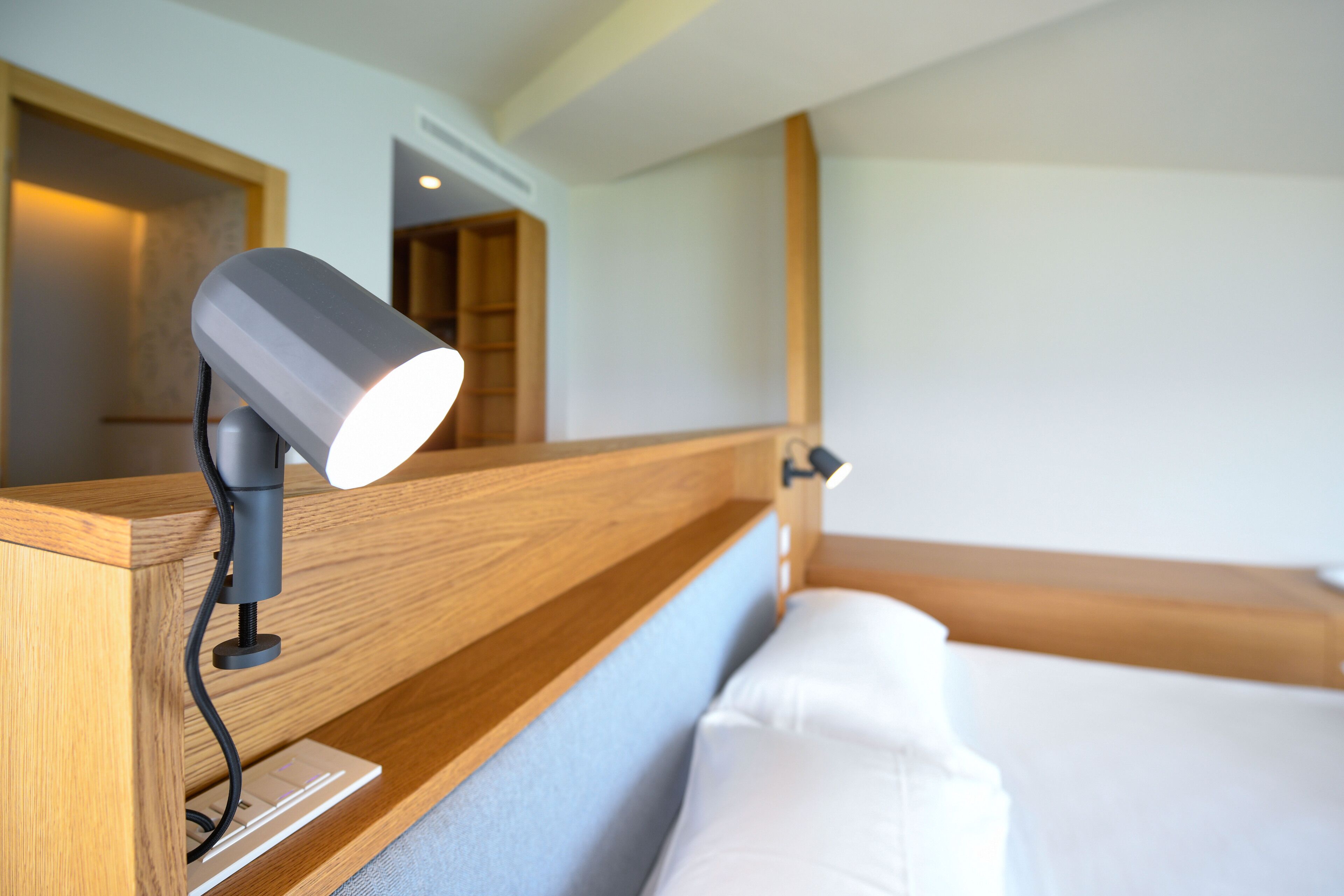 Une chambre d’hôtel avec une tête de lit en bois, une lampe de chevet et un lit avec une literie blanche.