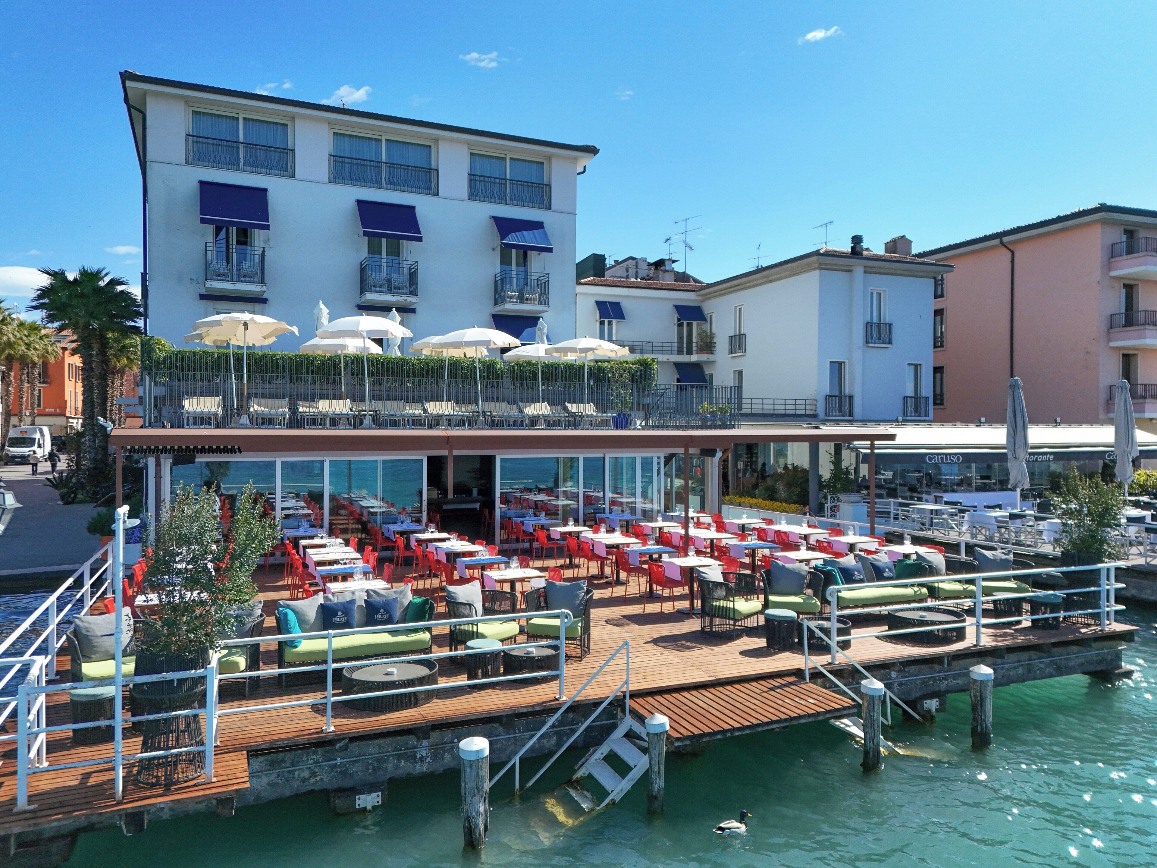 A waterfront restaurant with outdoor seating, a wooden deck, and a view of the water.