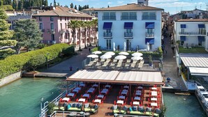 A riverside restaurant with outdoor seating, a dock, and a view of the cityscape. - Hotel Flaminia (Sirmione)
