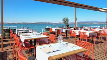 An outdoor dining area with tables and chairs, overlooking a body of water.