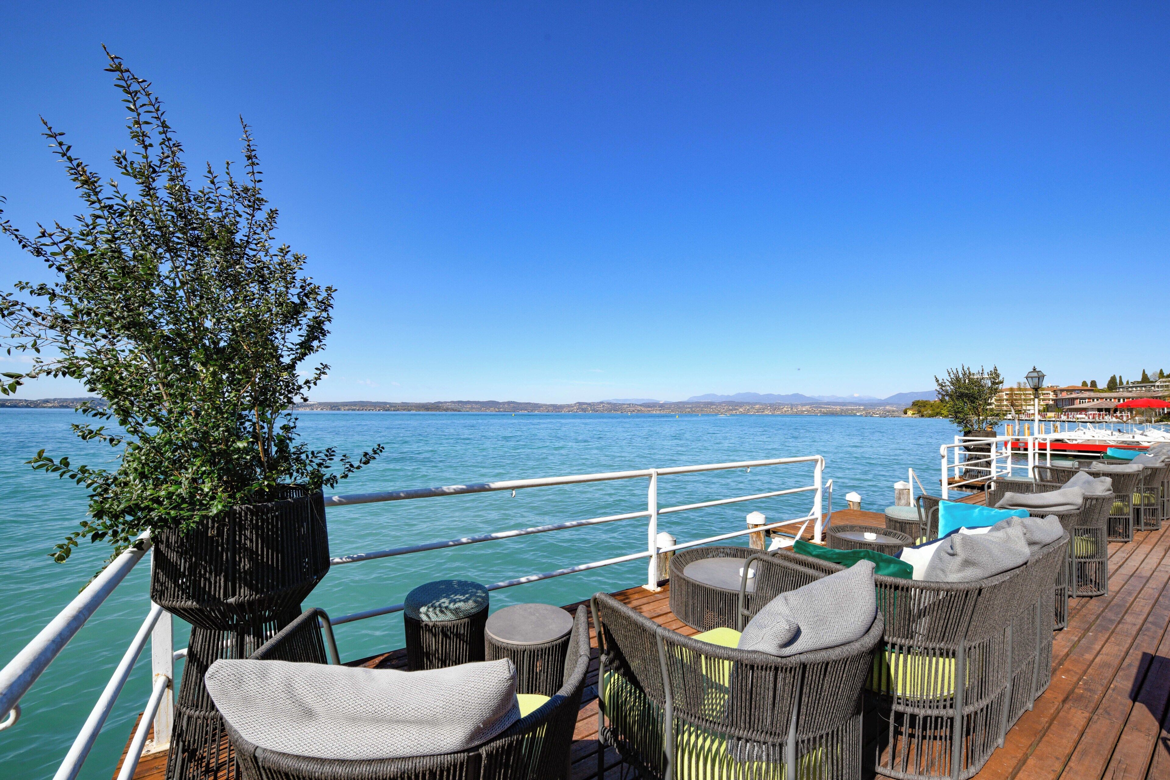 Eine Terrasse mit Korbmöbeln, einem Blumentopf und Blick auf das Wasser.