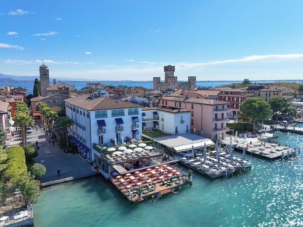 Un hotel frente al mar con terraza al aire libre, un puerto deportivo y edificios históricos.