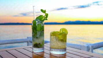 Two cocktails on a wooden table with a scenic view of a sunset over water.