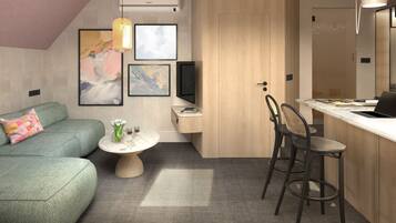 A modern living room with a green sofa, a round coffee table with flowers, and a dining area with two chairs and a laptop.