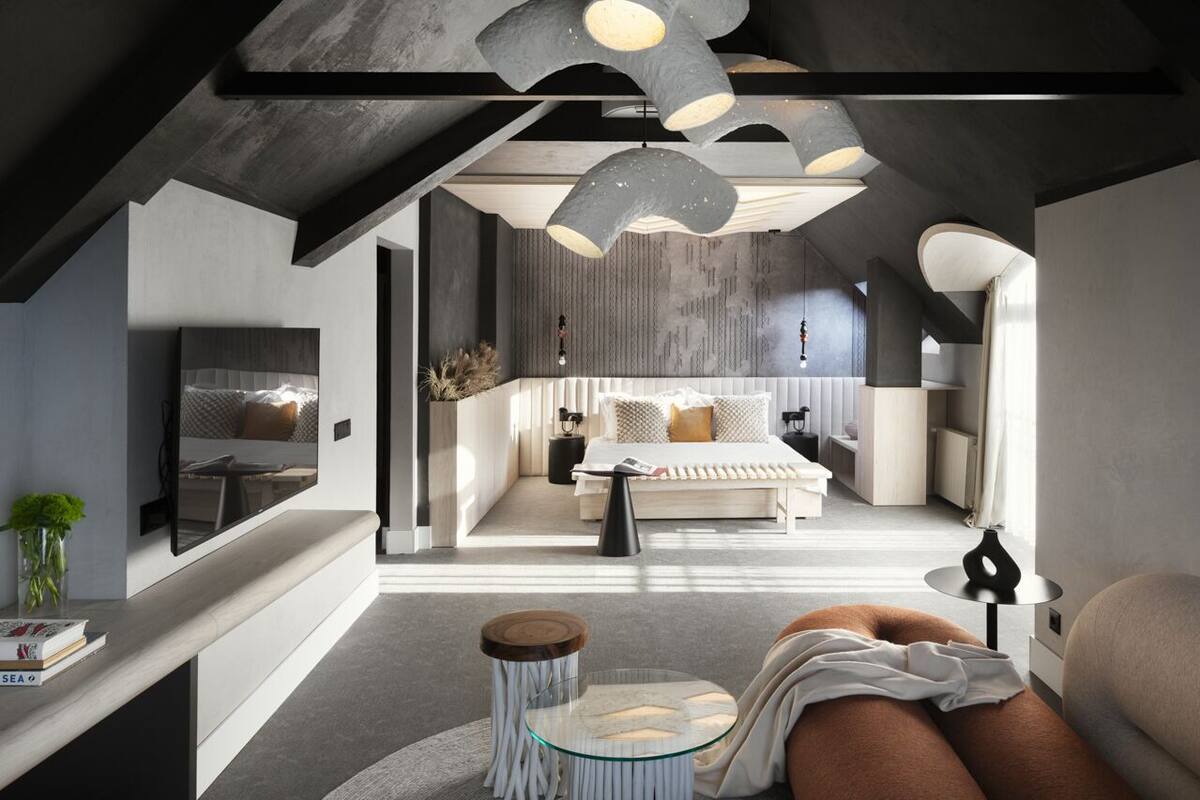 Una habitación de hotel moderna con una cama grande, un área de descanso con una mesa de vidrio y un diseño de techo original.
