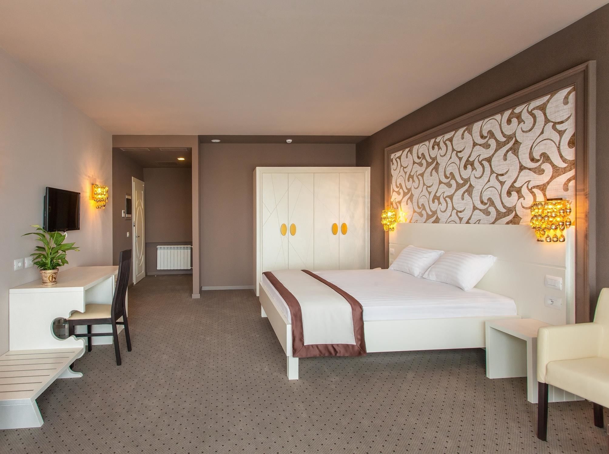 Habitación de hotel con cama, mesita de noche, silla, escritorio y televisor.