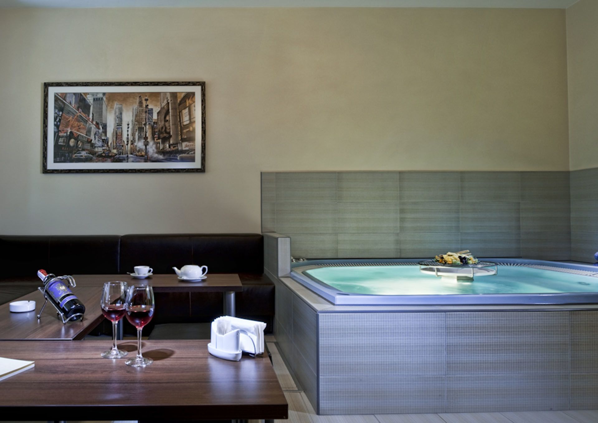 Une chambre d’hôtel avec une grande baignoire, une table à manger avec des verres à vin, une bouteille de champagne et un tableau au mur.