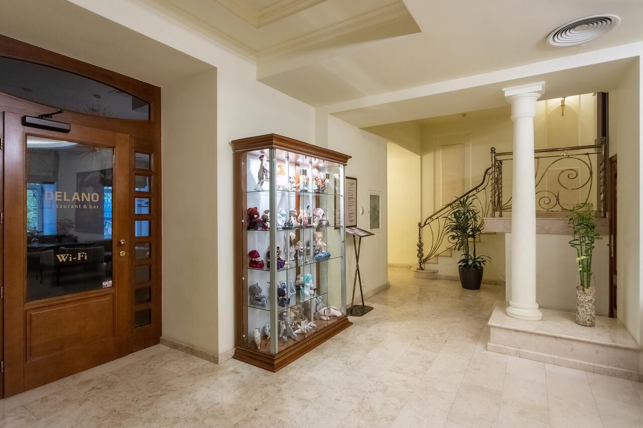 A hallway with a wooden door labeled "DELANO restaurant & bar," a glass display case with figurines, a staircase with a metal railing, and a potted plant.