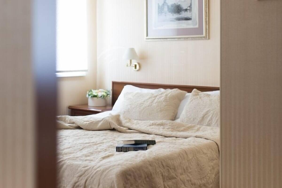 Habitación de hotel con cama, mesita de noche, un cuadro en la pared y una ventana con cortinas.