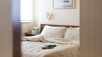 A hotel room with a bed, a nightstand, a framed picture on the wall, and a window with curtains.