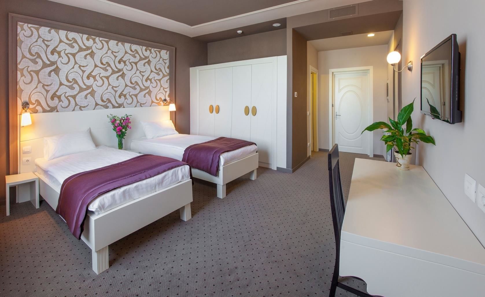 A hotel room with two beds, a desk, a wardrobe, and a bathroom visible through an open door.