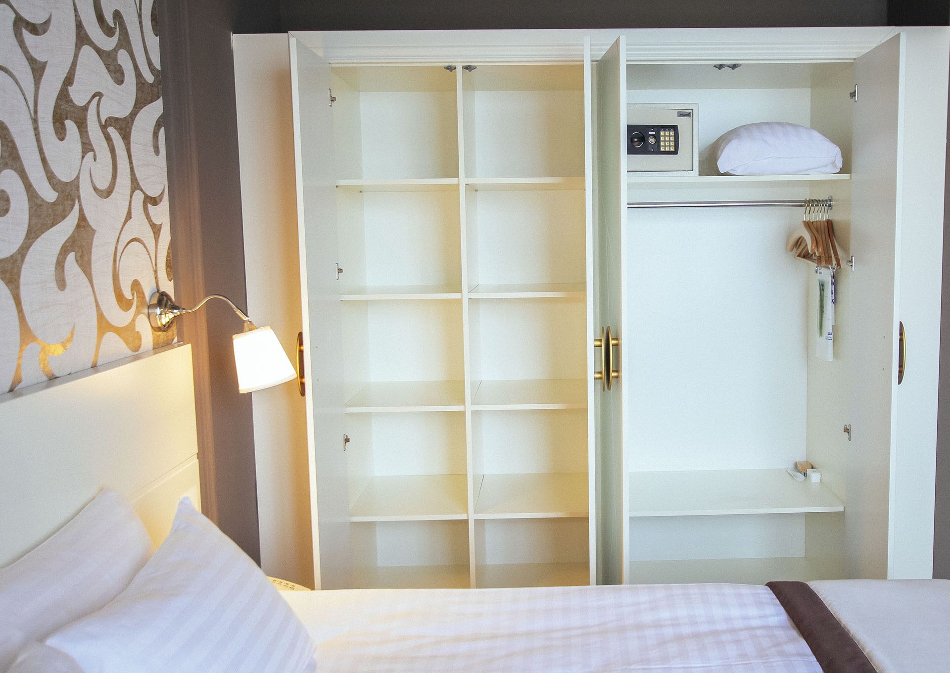 A hotel room with a large walk-in closet, a bed with white bedding, and a wall-mounted lamp.
