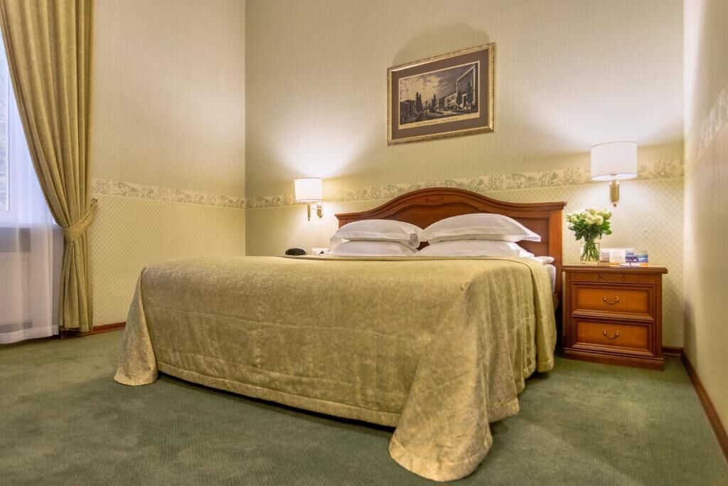 A hotel room with a large bed, two bedside lamps, a nightstand with a vase of flowers, and a framed picture on the wall.