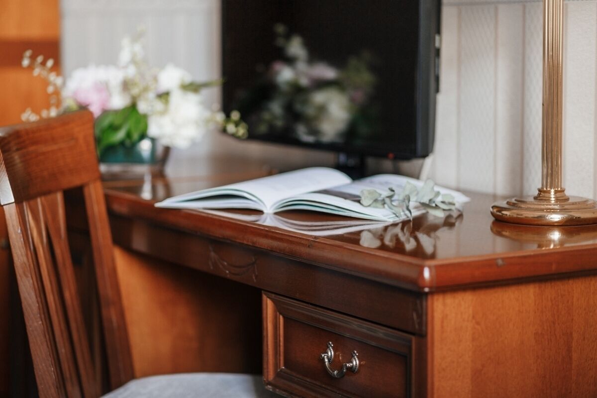 A wooden desk with an open book, a lamp, and a chair.