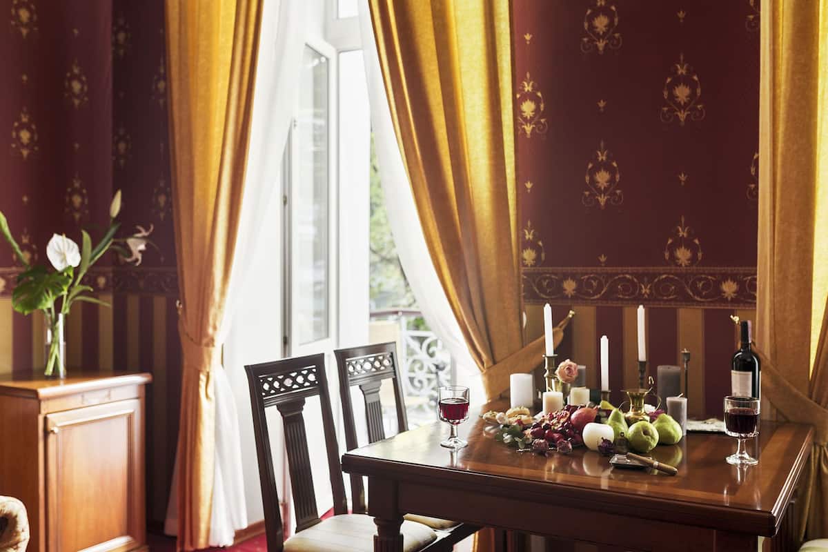 Una mesa de comedor con velas, flores y copas de vino, frente a una pared decorada con un ventanal y cortinas.