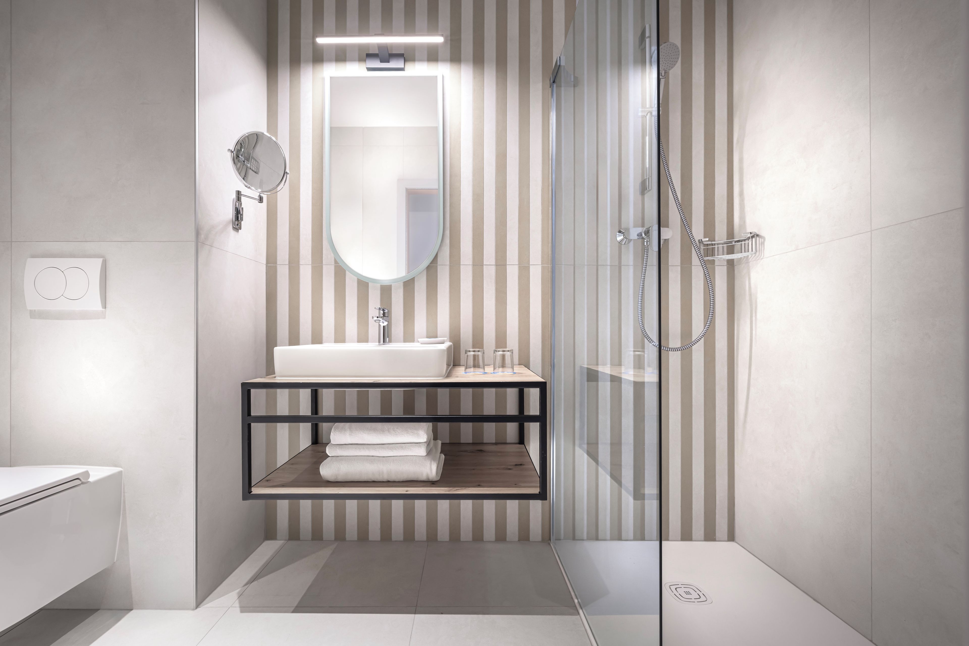 A modern bathroom with a glass shower enclosure, a white sink, and a striped wall design.