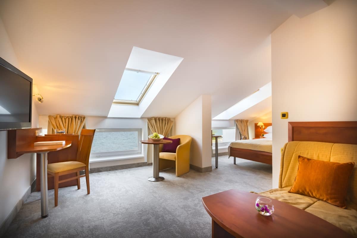 A hotel room with a bed, a desk, a chair, a small table, and a TV.
