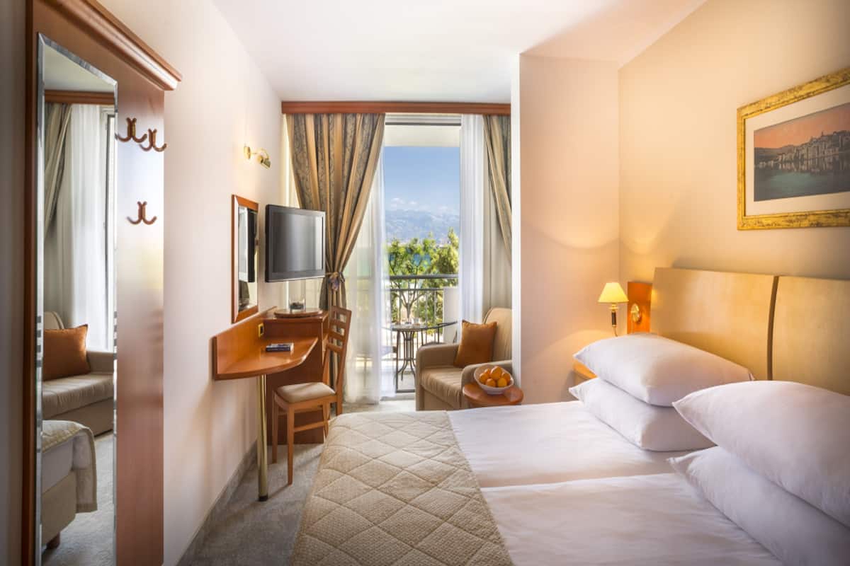 A hotel room with a bed, a desk with a chair, a television, a small table, and a balcony with a view.
