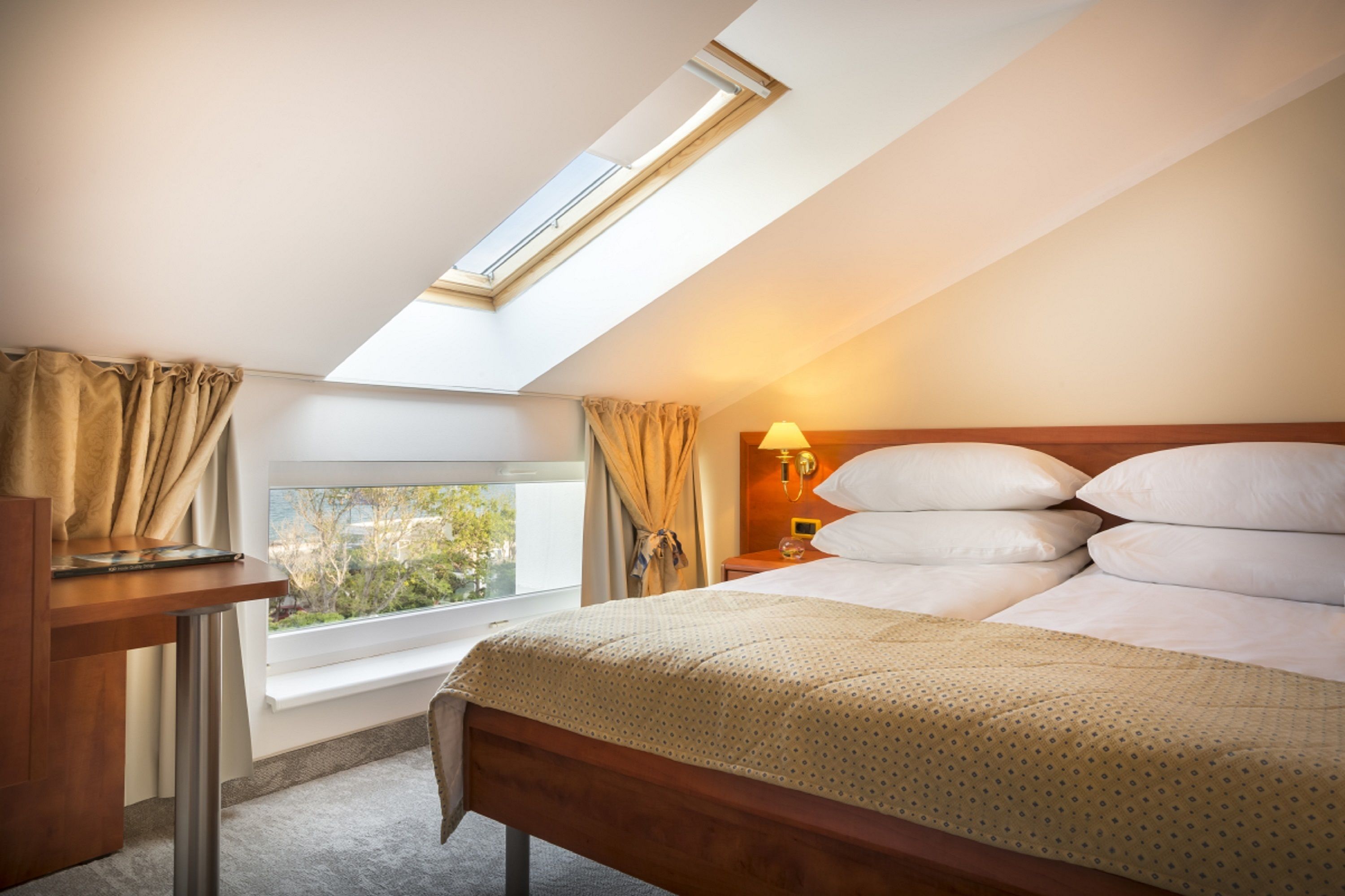 Een slaapkamer met dakraam, een bed met witte lakens, een nachtkastje en uitzicht op groen.