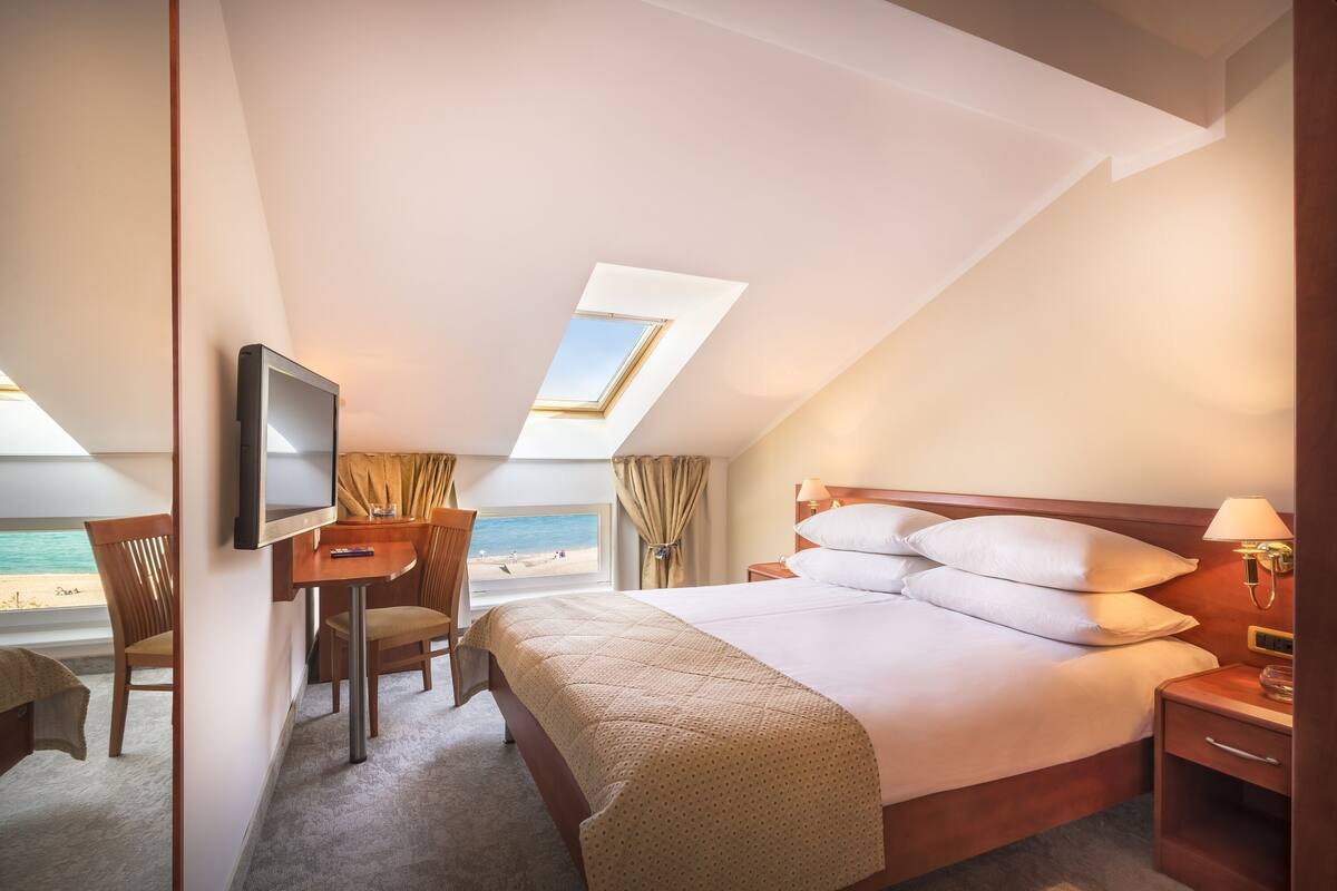 A hotel room with a bed, a desk, a television, and a view of the beach.