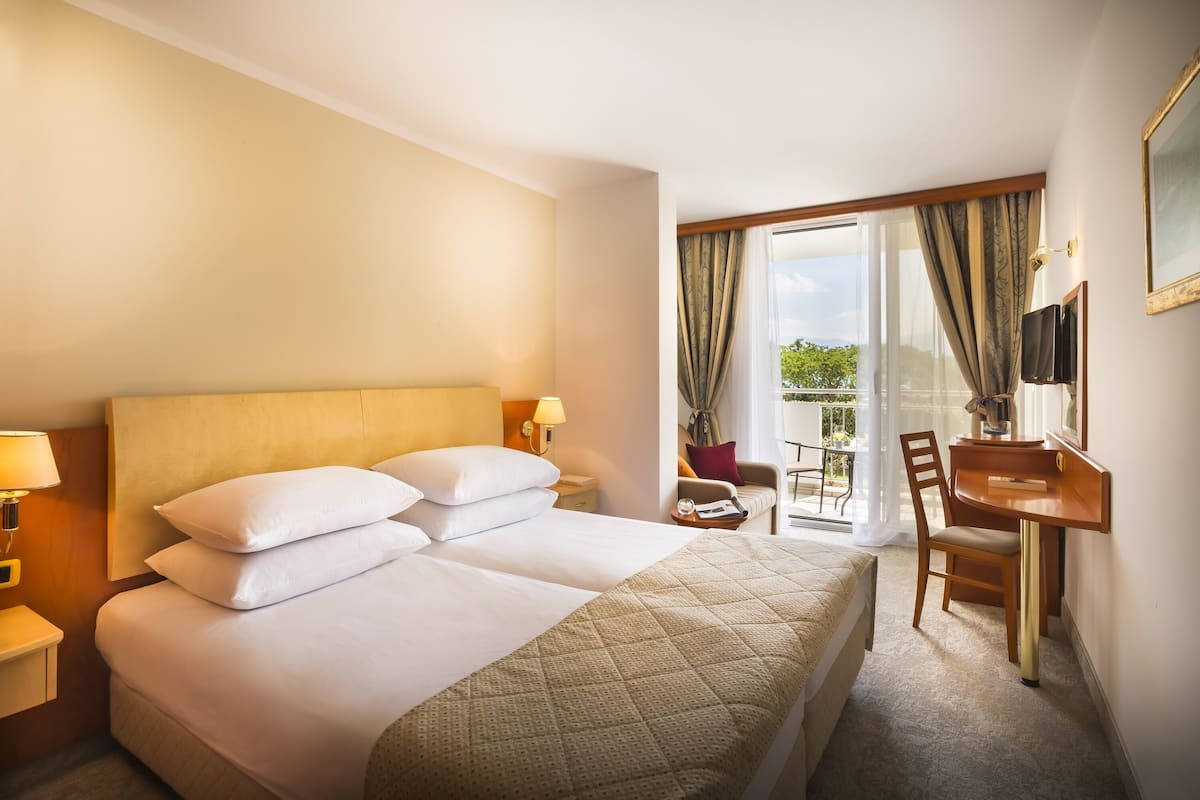 A hotel room with a large bed, a desk, a chair, and a view of the outdoors.