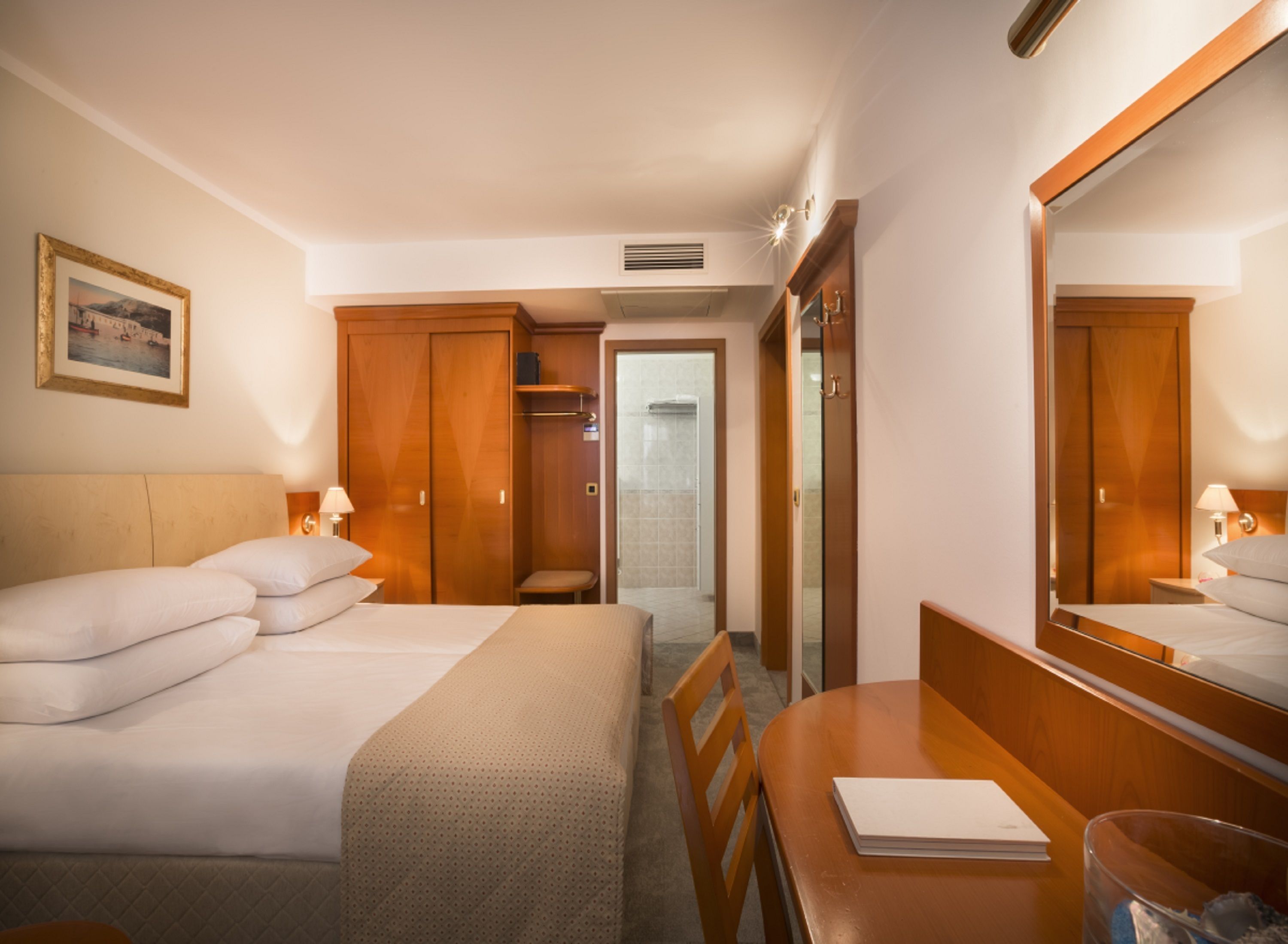 A hotel room with a bed, a desk, a chair, a mirror, and a wardrobe.
