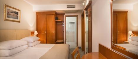 A hotel room with a bed, a desk, a chair, a mirror, and a wardrobe.