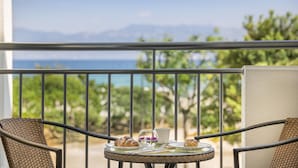 Un balcon avec une table dressée pour deux personnes, offrant une vue panoramique sur la mer et les montagnes.
