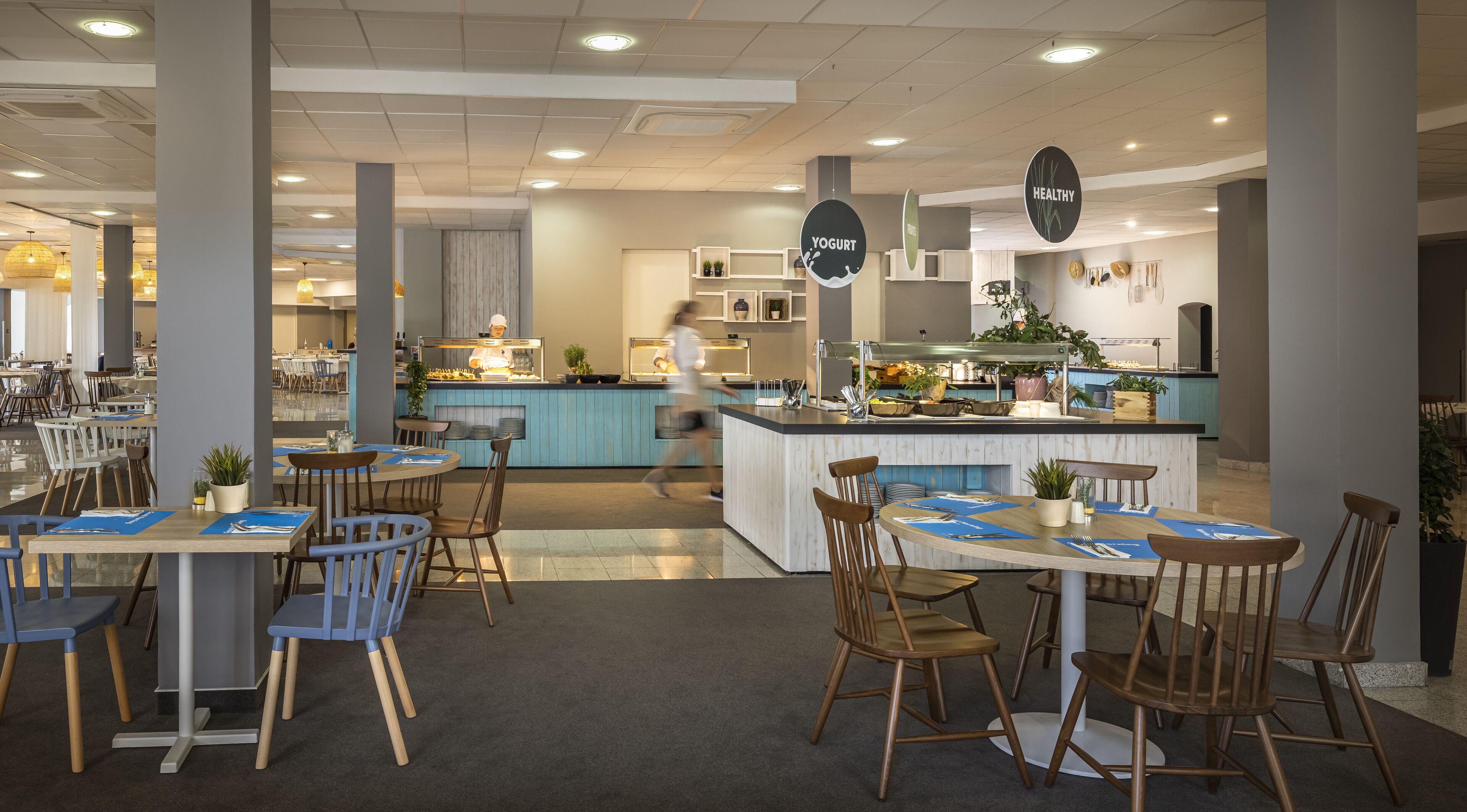 Een modern restaurant met een centraal eiland, zitgedeeltes met tafels en stoelen, en een zichtbare keuken.