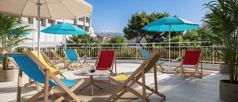 Een terras met meerdere lounge stoelen en parasols, een kleine tafel en potplanten.