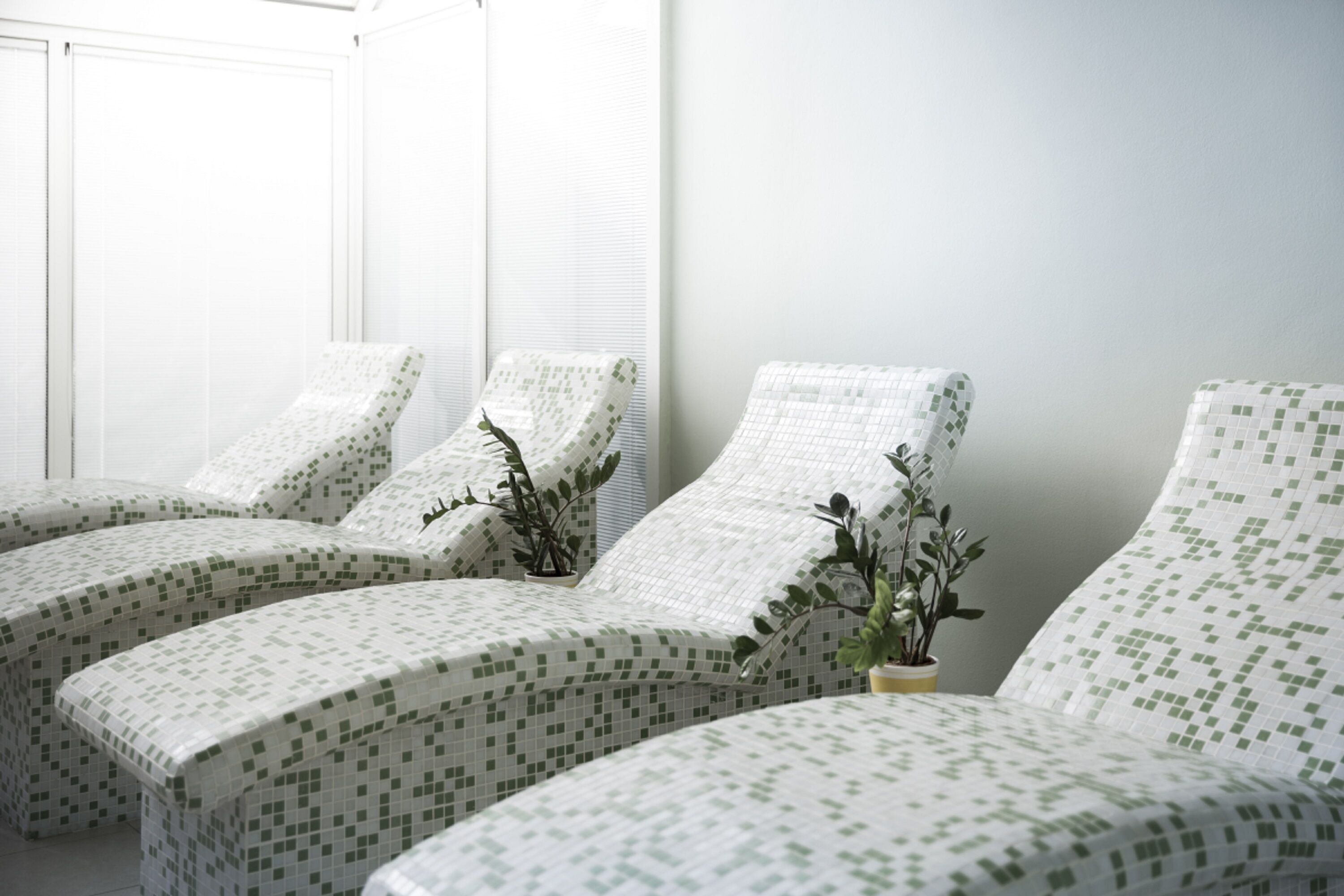 A room with three reclining chairs covered in a green and white patterned fabric, each with a potted plant.