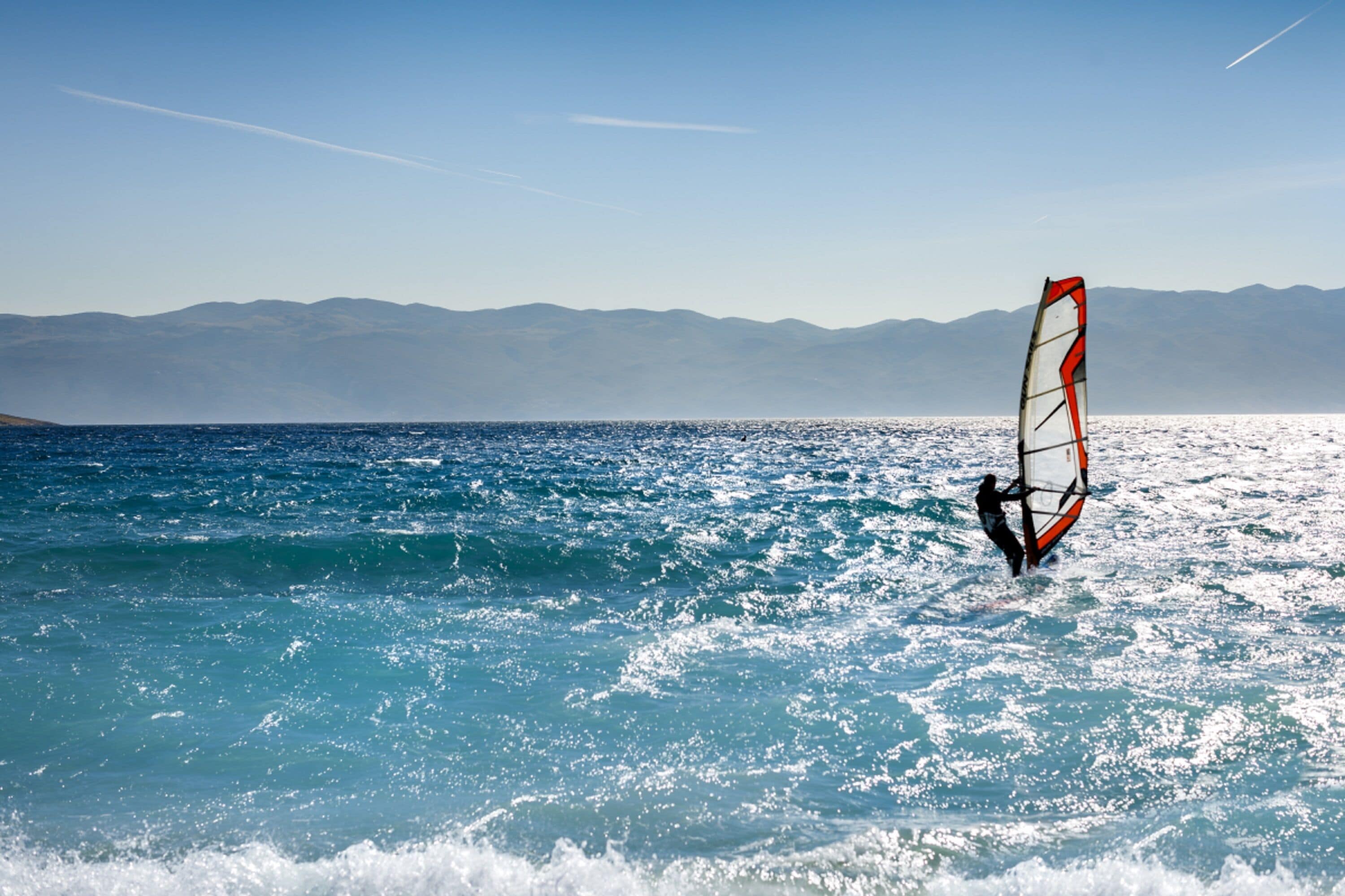 A person windsurfing on a clear day with mountains in the background.