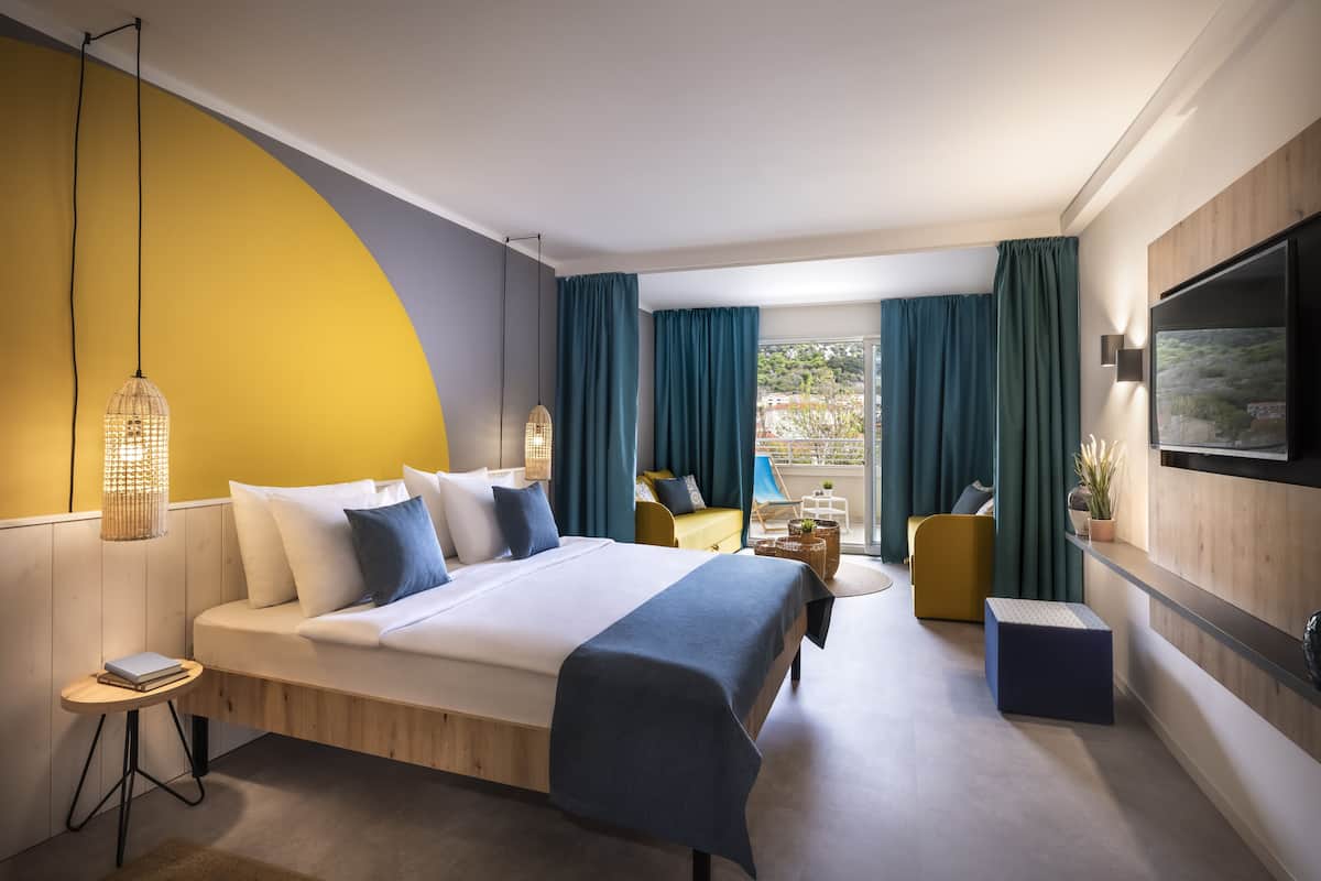 A modern hotel room with a bed, a small table, a sofa, and a TV mounted on the wall.